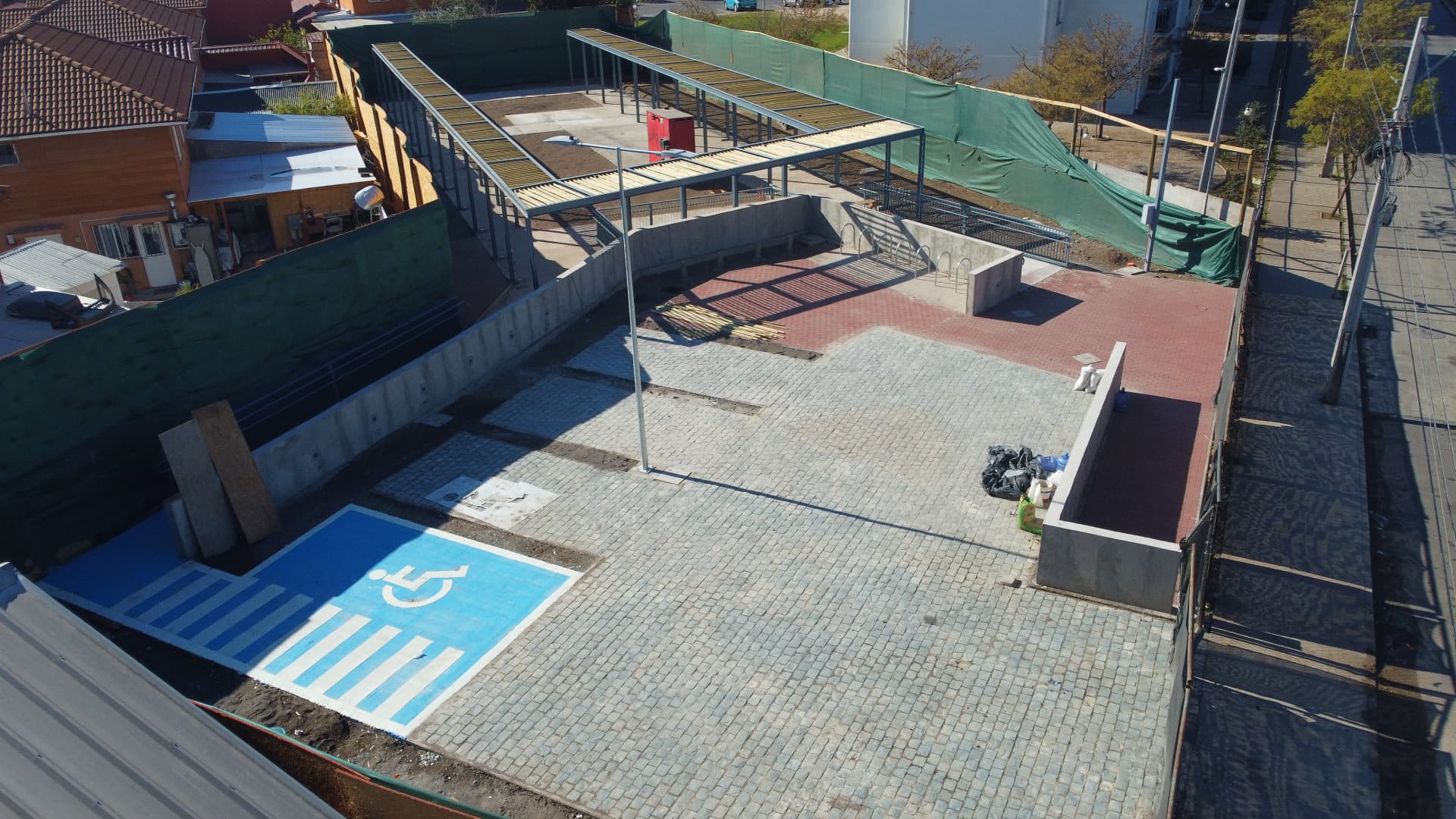 Vista aérea de plaza con pavimento de adoquín, estacionamiento accesible y estructura metálica